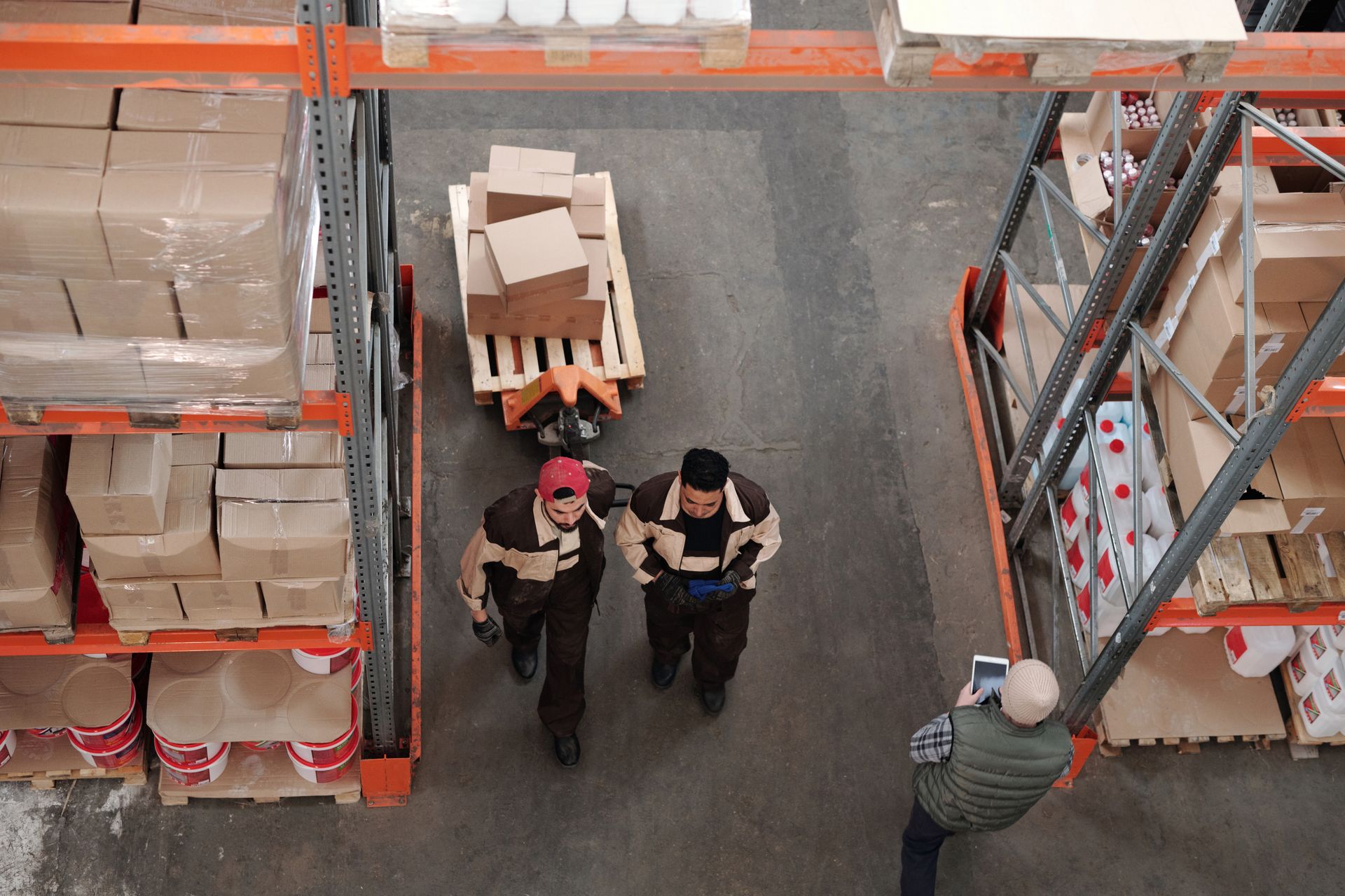 Warehouse crew moving stock on a pallet jack between loaded racks